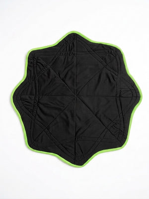Introducing the Astral Dapo—a black, star-shaped quilted mat with a vibrant green border, shown flat on a white surface. This bold festival accessory infuses any gathering with playful cosmic planetary print energy.