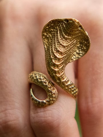 A gold adjustable Sarpa Coil Ring shaped like a cobra hood worn on a finger.