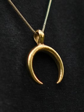 The Chandra Talisman features a gold crescent moon pendant on a delicate chain, radiating bohemian charm as it’s showcased against a black background.