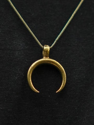 The Chandra Talisman—a gold crescent moon pendant on a fine chain—rests against black fabric, making this elegant lunar necklace ideal for bohemian jewelry lovers.