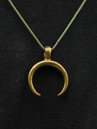 The Chandra Talisman—a gold crescent moon pendant on a fine chain—rests against black fabric, making this elegant lunar necklace ideal for bohemian jewelry lovers.