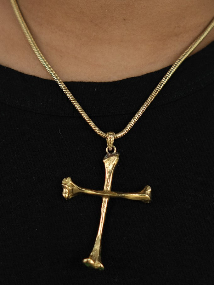 The Eternal Relic Necklace features a gold pendant shaped like two bone-like pieces, creating an eye-catching gothic look when worn over a black shirt.