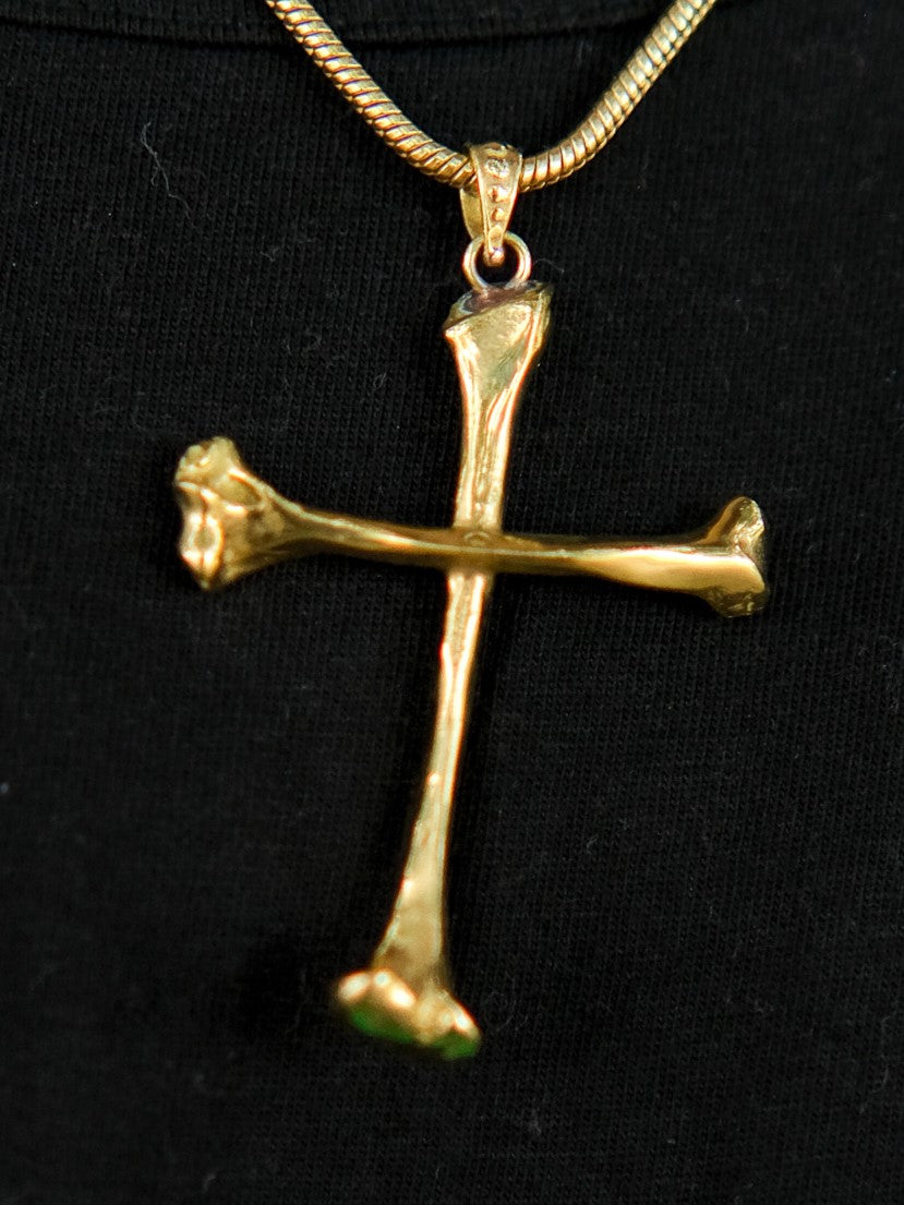 The Eternal Relic Necklace in gold features a pendant of two bone-like pieces, displayed on black fabric—a striking choice for gothic jewelry enthusiasts.