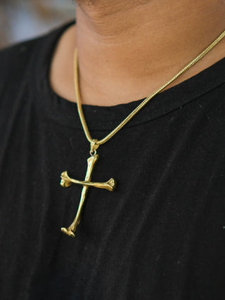A person wearing a black shirt and the Eternal Relic Necklace—gothic jewelry with a gold pendant featuring a cross made from two intertwined bones.