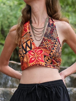 Wearing the Tribal Bloom Top with its vibrant geometric and floral patterns, paired with black pants and a layered necklace, this look stands out against a lush green backdrop—ideal summer festival attire.