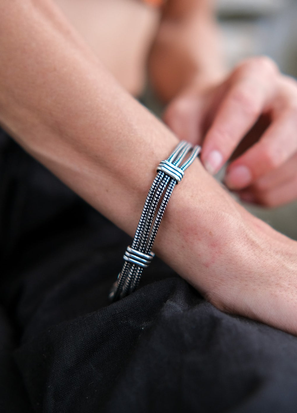 A close-up of a person’s wrist adorned with the Shakti Lines Bracelet, showcasing its stylish black and silver bohemian design as their hand gently touches it, set against a blurred background.