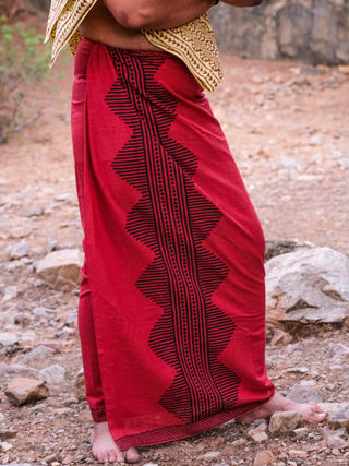 Barefoot on rocky ground, a person wears an Anviksha Dhoti featuring black geometric patterns with hints of gold, capturing the spirit of traditional Indian attire.