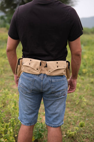 A person wearing a black t-shirt, blue denim shorts, and the Verdant Multi-Pocket Utility Belt Bag featuring tribal geometric accents stands outdoors on grass, facing away from the camera.