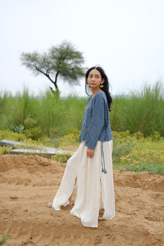 A woman wearing the Bohemian Long-Sleeve Top and a white skirt stands on sandy ground with green grass and a tree in the background, looking over her shoulder.