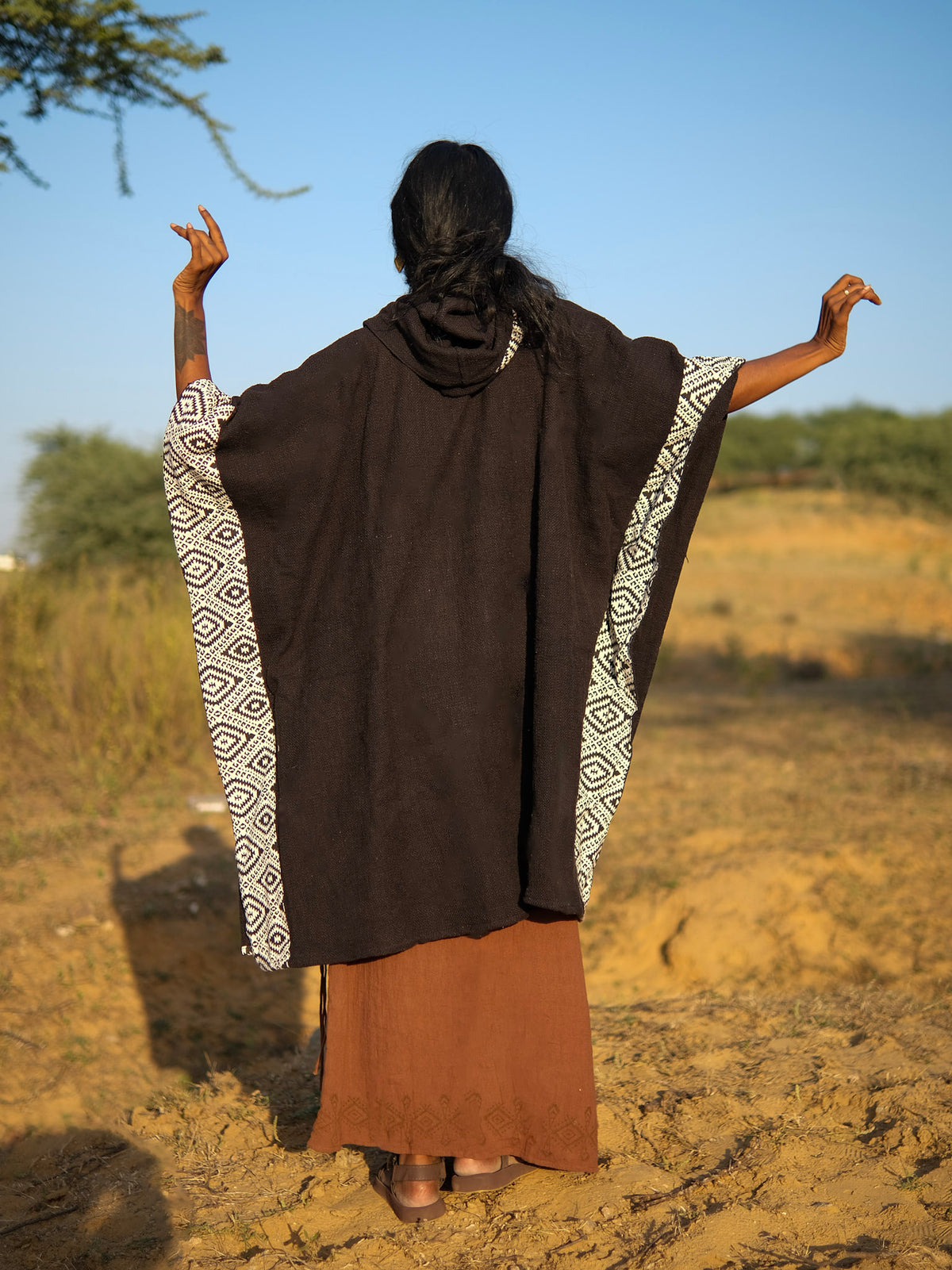 A person seen from behind wearing a black Neer poncho with a geometric white pattern along the sides.