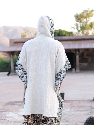 A person viewed from behind wearing a Neer Poncho, a light-colored boho style featuring black and white geometric patterned accents on the hood and sides.