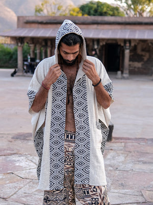 A person wearing an open, hooded Neer Poncho featuring black and white geometric patterns, layered over patterned shorts.