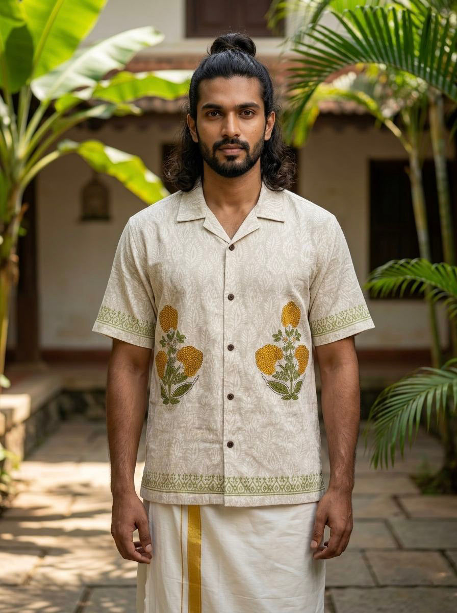 A man with long hair tied up, wearing the Natural Sunehri Shirt styled with a traditional dhoti, stands outdoors between tropical plants and a building.