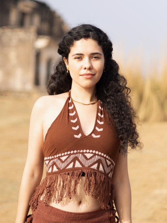 Wearing the Divine Crop Top, a woman with long curly hair stands outdoors in sunlight, with dry grass and old buildings softly blurred in the background.