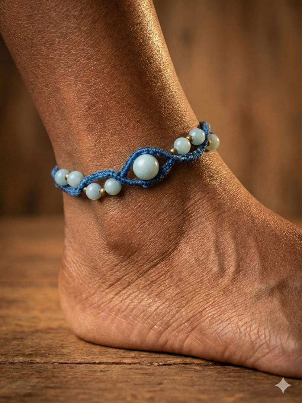 A close-up of an ankle adorned with the Aarohi Aventurine Boho Anklet, featuring light blue round beads and blue beaded details, set against a wooden floor and brown background.