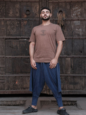 Full-length view of the blue Aabroo Pant worn with a brown tee against a wooden backdrop