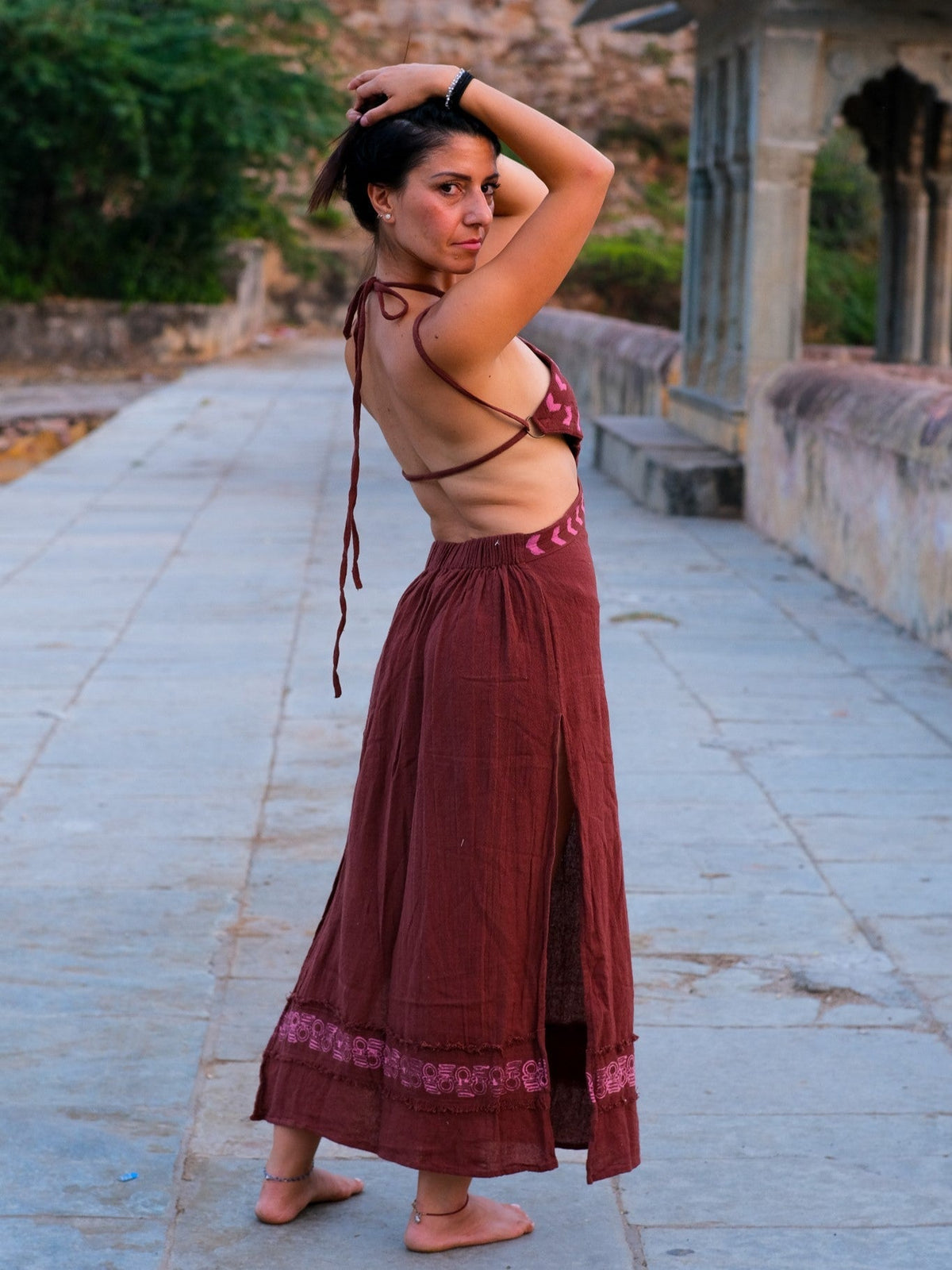 Aadhya maroon block print maxi dress with arms raised behind her head in a palace courtyard