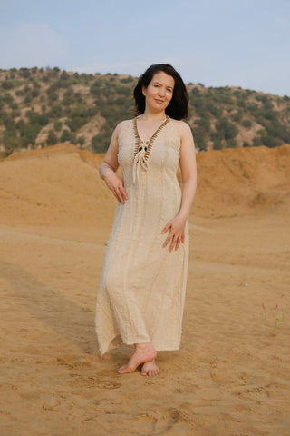 Aaven Crossback Dress in natural cream, relaxed one-size maxi with hand-knotted front lacing, worn on sand