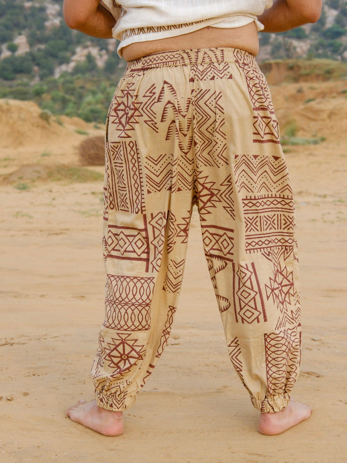 Back view of beige cotton harem pants with brown hand block printed tribal motifs, elastic waist and gathered cuffs