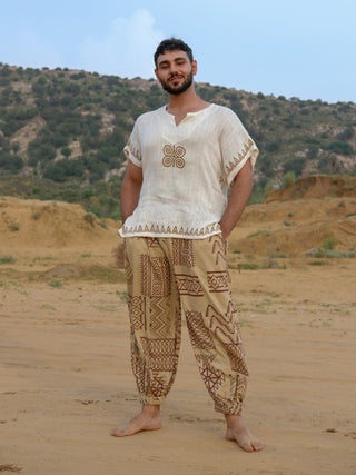 Man in full length beige hand block printed harem pants with brown tribal motifs and gathered ankle cuffs, desert dunes
