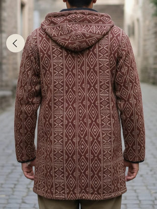 Back view of the maroon and cream Adivasi hooded jacket worn down a cobbled street between stone buildings