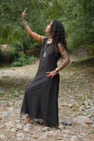 Afra Maxi Dress black colourway with arm raised in forest stream landscape