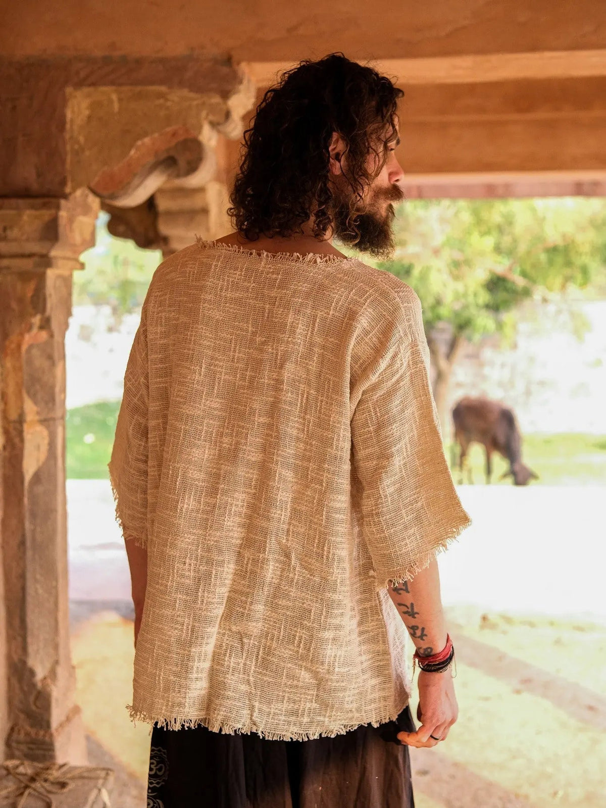 Beige cotton-jute baggy T-shirt back view in a stone corridor, showing the raw frayed back hem