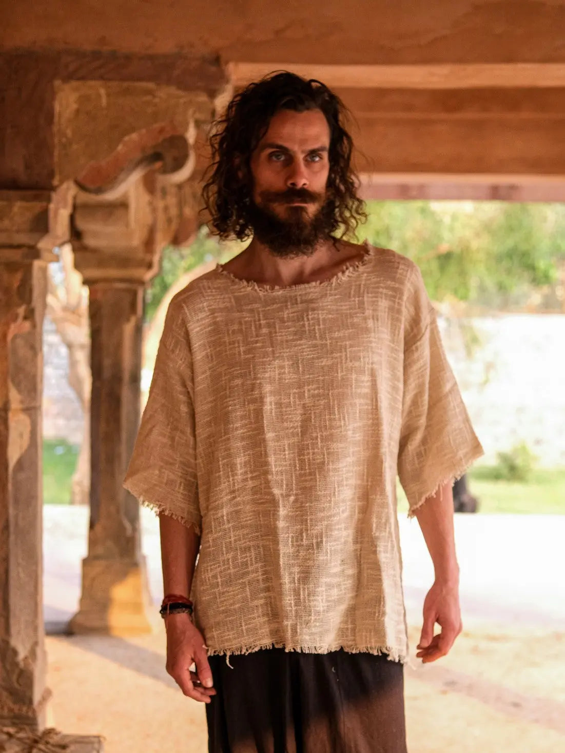 Beige cotton-jute baggy T-shirt front view in a warm stone corridor, raw frayed neckline and hem
