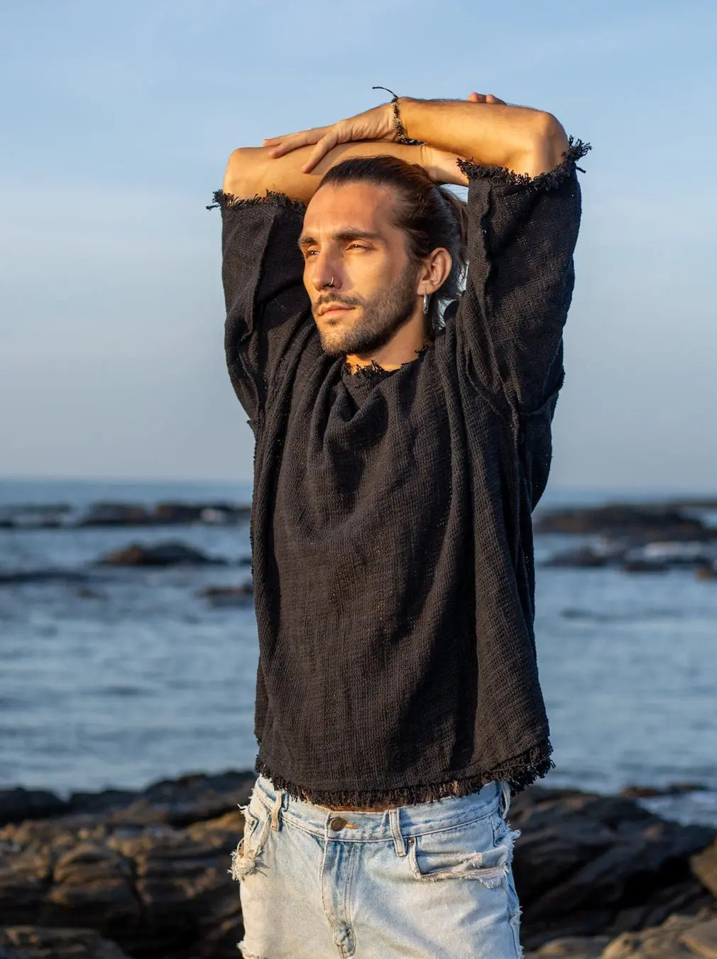 Black baggy jute T-shirt with arms raised overhead, showing the frayed sleeve hems and relaxed body