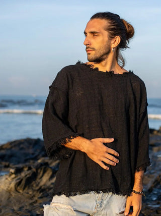 Black cotton-jute baggy knit T-shirt on a model at the shoreline, raw frayed neckline and sleeve hems, light blue jeans
