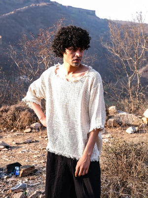 Cream cotton-jute baggy T-shirt against dry hills, raw frayed neckline and hem, open weave, black pants
