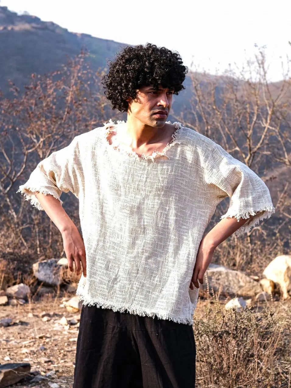 Natural cream baggy jute T-shirt worn hands on hips outdoors, open gauze weave and frayed hem, black pants