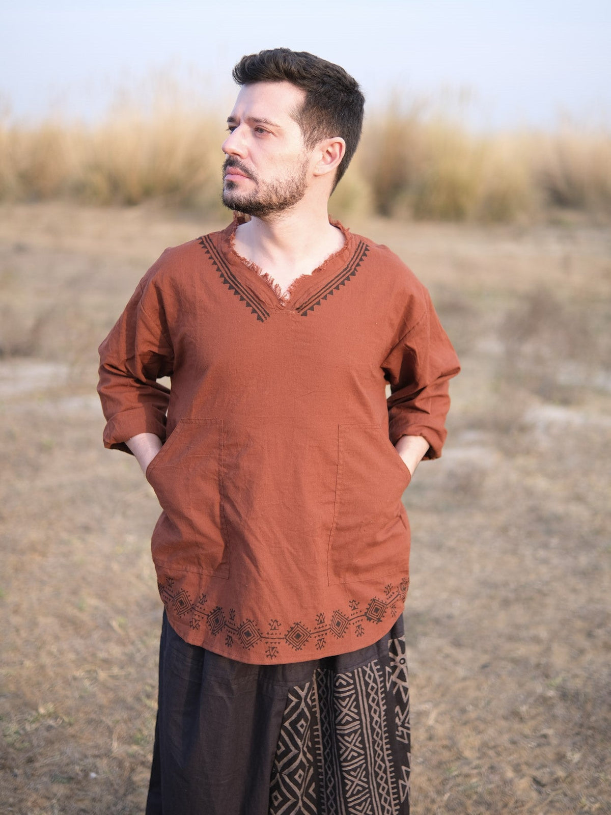 Rust baggy kurta with hands resting in the two front patch pockets, field backdrop