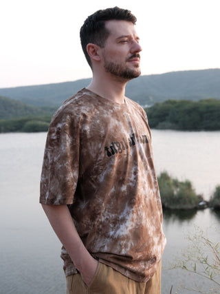 Side view of the Become the Light brown and cream tie-dye oversized tee by a lake, relaxed short sleeves.