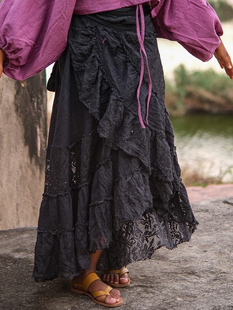 Front of the black layered wrap skirt with the tie cord hanging loose, openwork lace tiers against a riverside backdrop