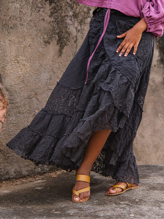 Black wrap skirt against an old plaster wall, folded waistband and tie cord visible above tiered lace ruffles