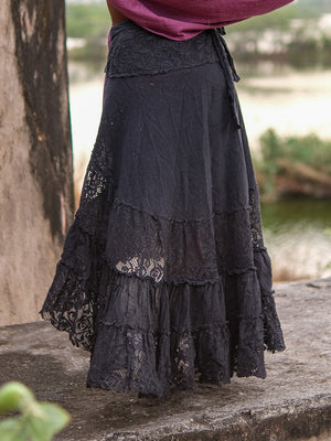 Close view of the black wrap skirt waist beside a river, crochet-style lace panel and knotted tie at the side