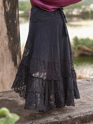 Close view of the black wrap skirt waist beside a river, crochet-style lace panel and knotted tie at the side
