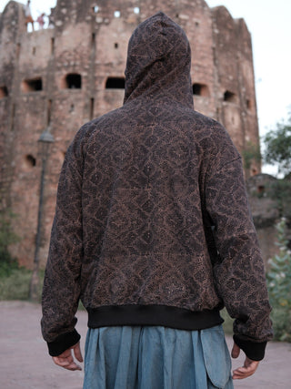Black maze-print hoodie, back view with hood up on male model, fort tower in background