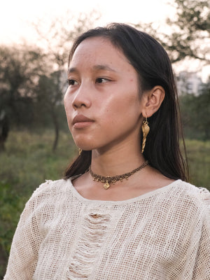 Three-quarter portrait of a model wearing the Brahman serpent earring outdoors, in a cream crochet top and beaded choker