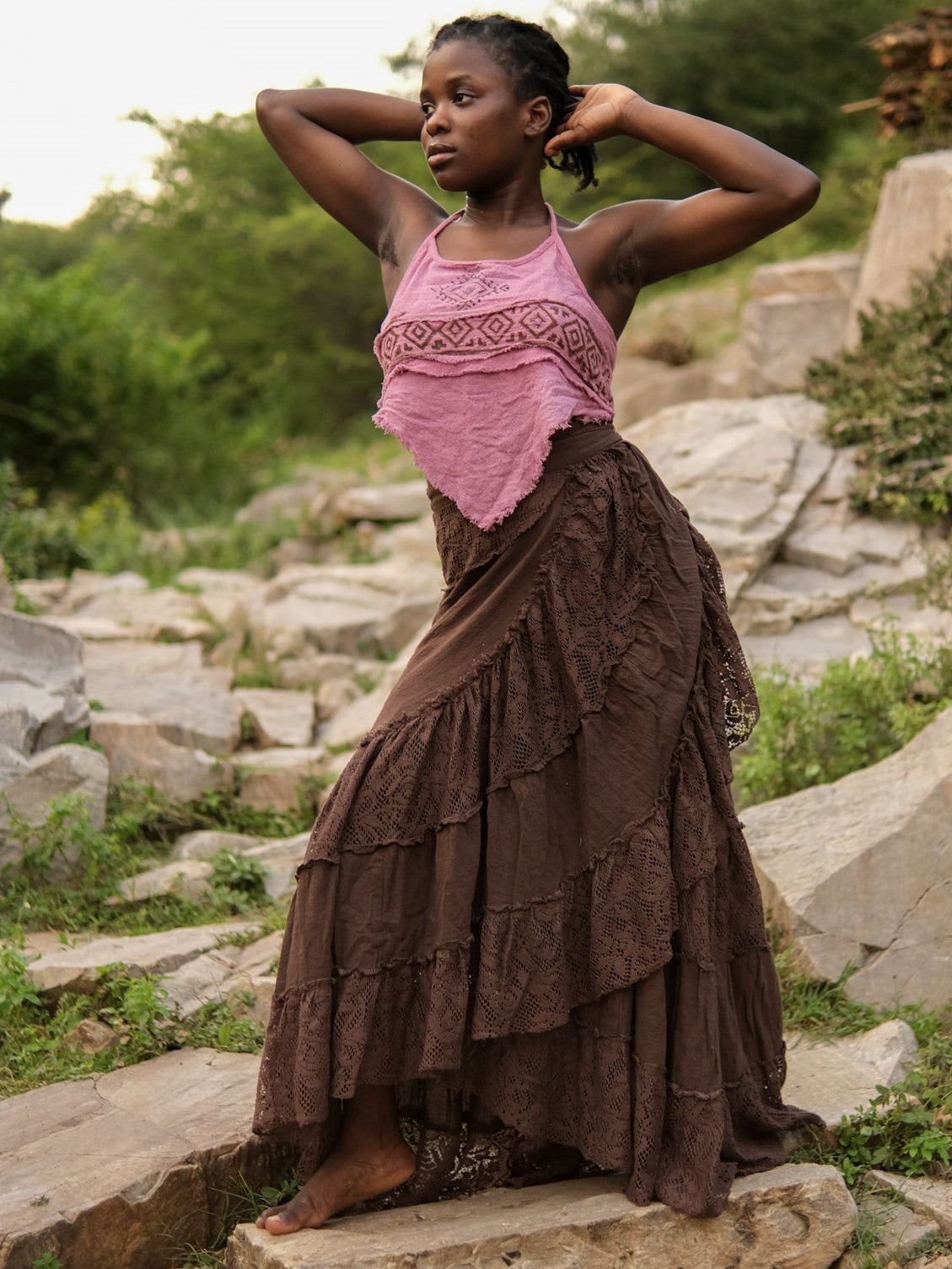 Brown khadi cotton gypsy wrap skirt on a model among grey rocks, tiered lace hem flaring as she turns