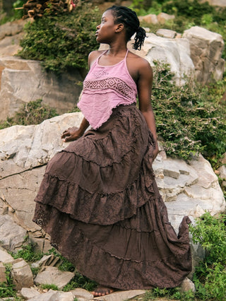 Model resting on rocks in a brown tiered gypsy wrap skirt, lace ruffle edges catching the light across her lap