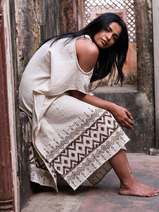 Chandra Kaftan seated on heritage steps, model in cream block print cotton jute kaftan with brown geometric hem
