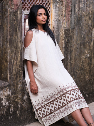 Chandra Kaftan side view, model seated against weathered stone wall, cream kaftan with brown block print border