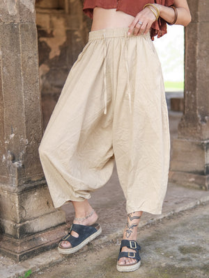 Warm beige cotton harem pants worn with a rust crop top and black sandals, standing among carved sandstone pillars.