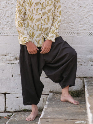 Black cotton harem pants worn seated on a white marble ledge with a leafy block print shirt, barefoot, legs gathered.