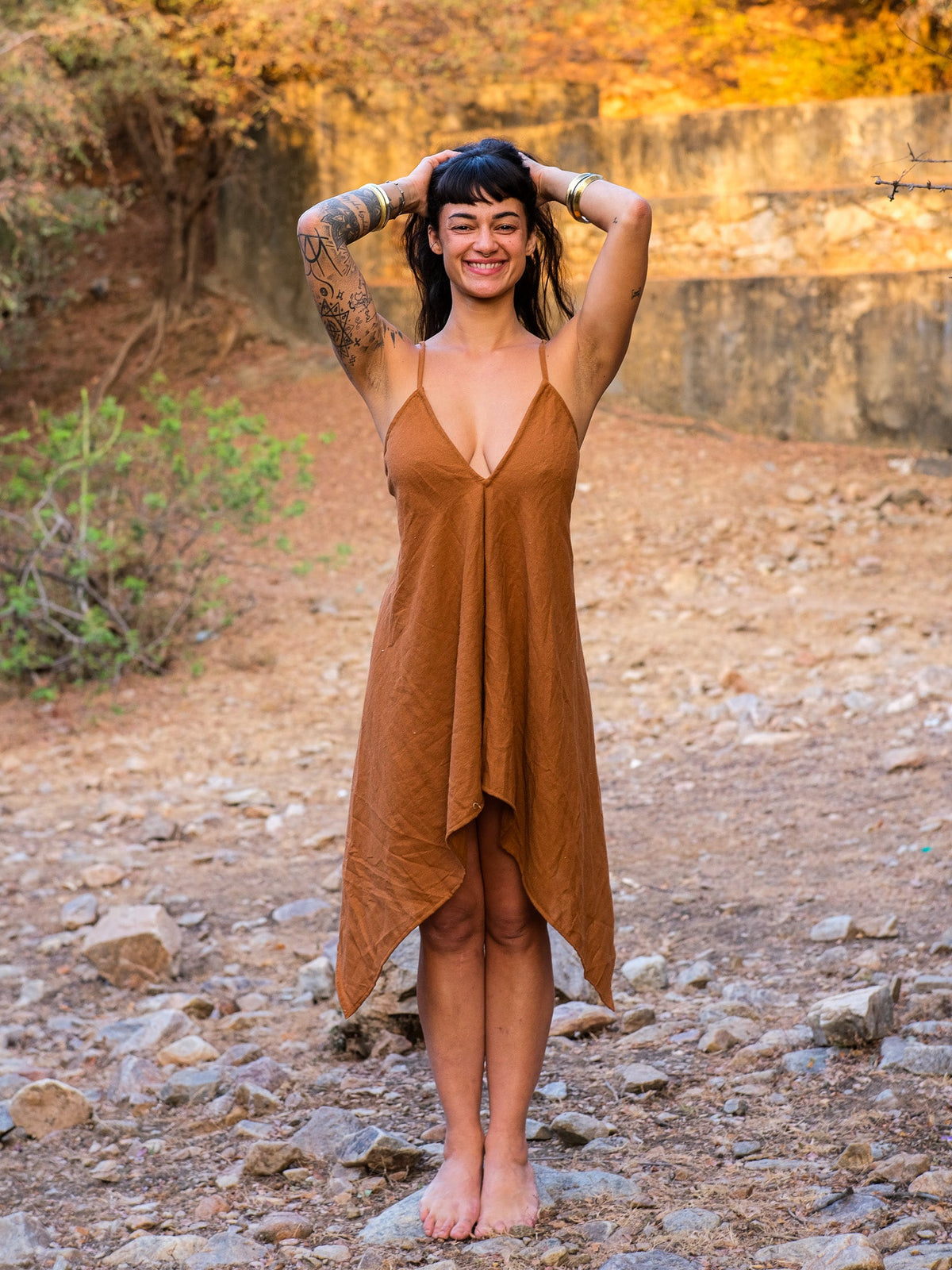 Dumati Dress in earthy brown cotton, front view on a barefoot model showing the deep V halter neckline and handkerchief hem