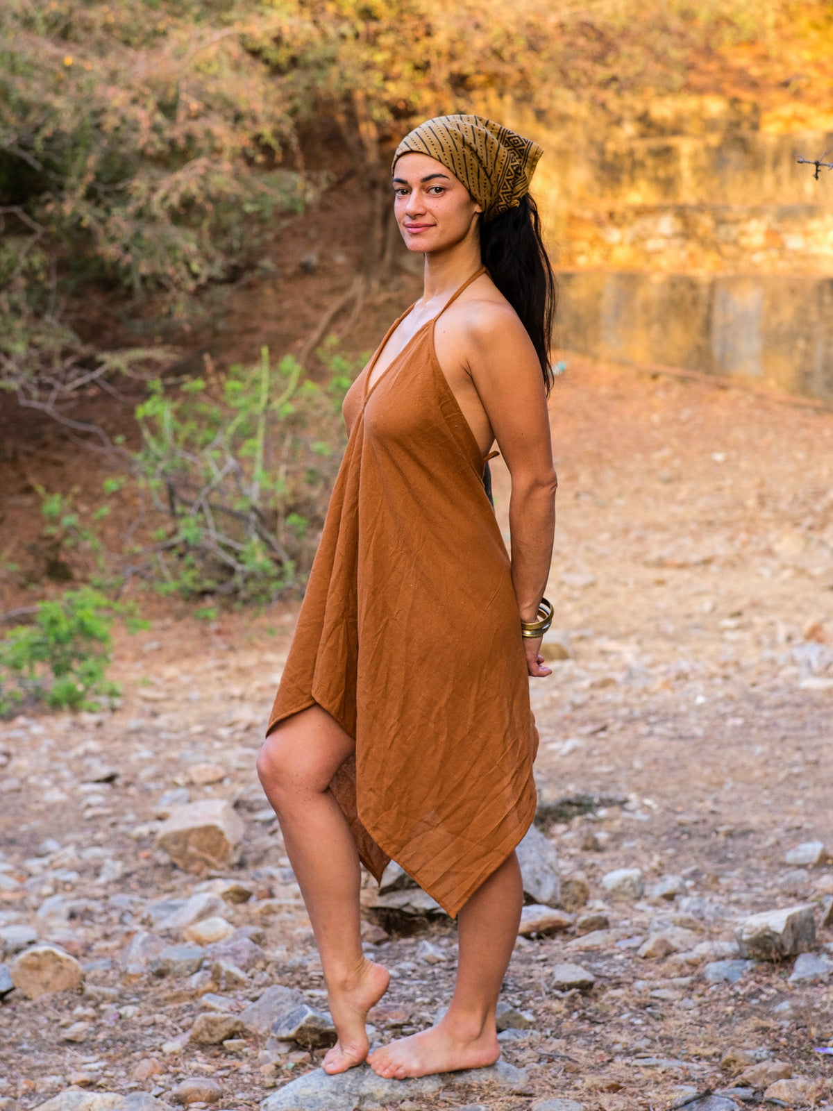 Dumati Dress boho cotton halter dress worn with a patterned headscarf, side view of the relaxed A-line on a rocky riverside