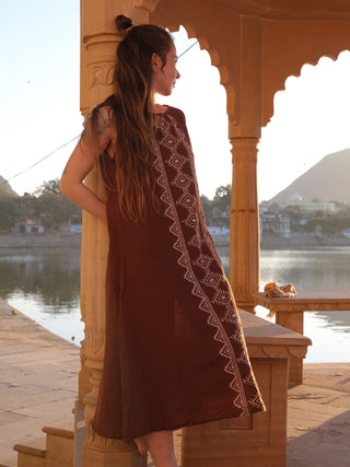 Ekakshi Maxi Dress in rust brown seen from the back at a carved pillar, showing the plain back panel