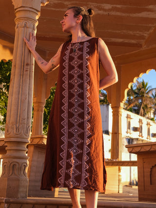 Ekakshi Maxi Dress in rust brown beside a temple pillar in warm golden light, print panel in view